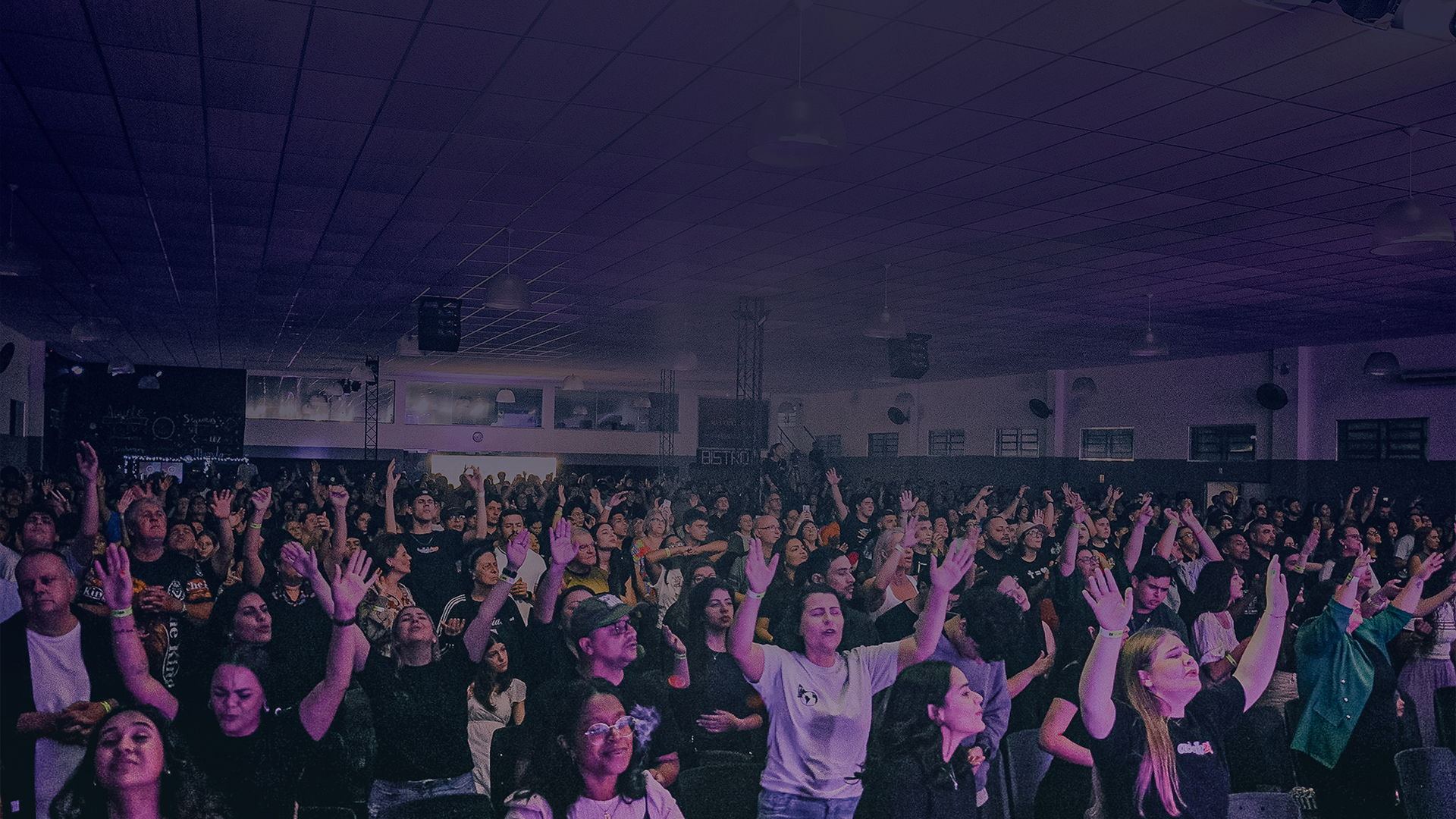 Salão cheio durante um culto, pessoas de mãos levantadas em adoração